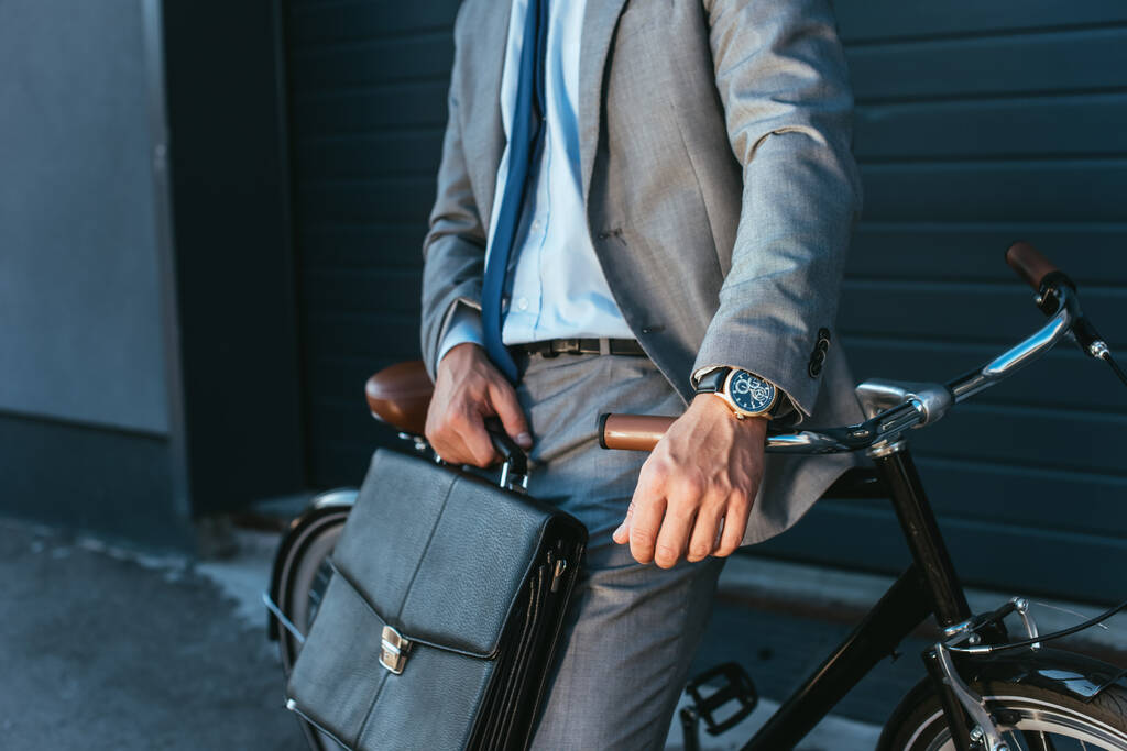 Περικοπή άποψη του επιχειρηματία με κοστούμι κρατώντας χαρτοφύλακα κοντά σε ποδήλατο σε εξωτερικούς χώρους  - Φωτογραφία, εικόνα