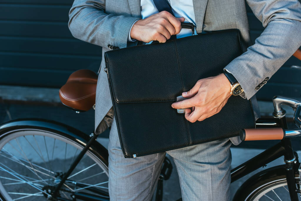 Cropped view of businessman locking briefcase beside bicycle outdoors  - Photo, Image