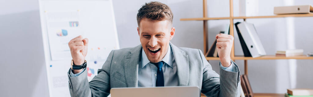 Pozitív üzletember mutatja igen gesztus közelében laptop elmosódott előtérben, banner  - Fotó, kép