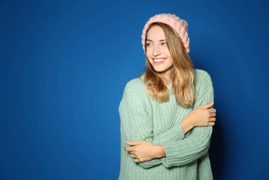 Szczęśliwa młoda kobieta w ciepłym swetrze i dzianiny kapelusz na niebieskim tle - Zdjęcie, obraz
