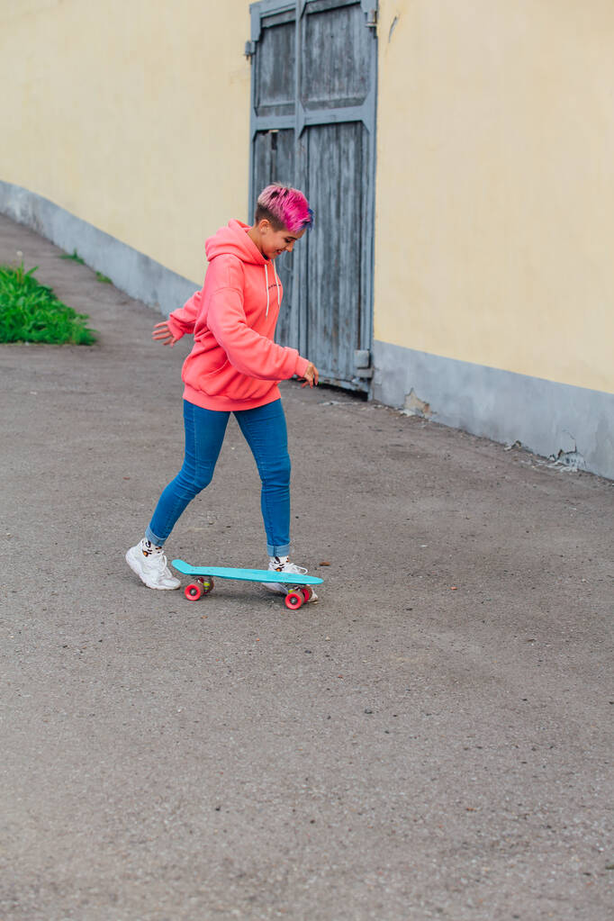 Стильная молодая женщина с короткими окрашенными волосами катается на голубом пластмассовом скейтборде. Концепция молодежи. - Фото, изображение