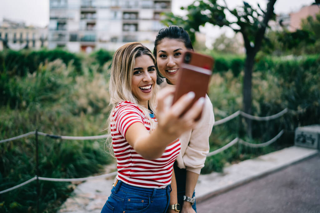 Усміхнені бікіні та азіатські дівчата-хіпстери позують на камеру смартфона, роблячи контент для блогу у вільний час, щасливі молоді 20-ті жінки розважаються у вільний час у Томі, беручи селфі через додаток на мобільний телефон
 - Фото, зображення