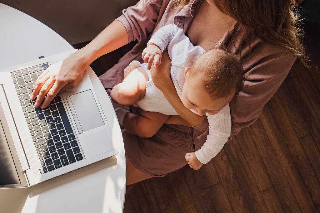 Young mom working remotely on laptop while taking care of her baby. - Photo, Image