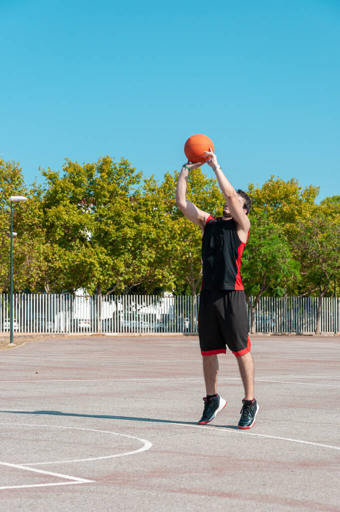 Basketbol potasına top atan genç bir adamın dikey çekimi. - Fotoğraf, Görsel