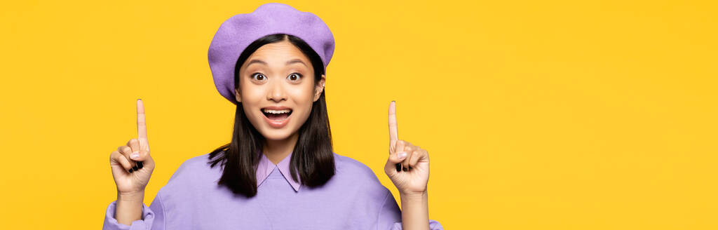 onnellinen aasialainen nainen baskerissa osoittaa sormilla eristetty keltainen, banneri - Valokuva, kuva