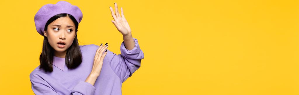 aasialainen nainen baskerissa osoittaa mitään elettä kädet eristetty keltainen, banneri - Valokuva, kuva