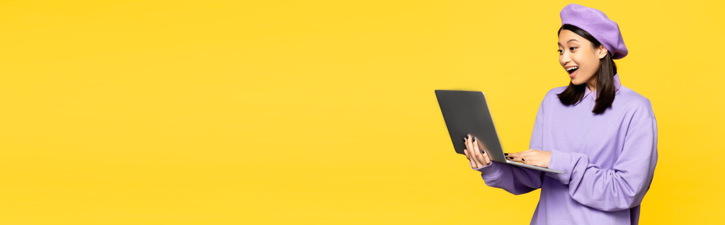 feliz mulher asiática na boina usando laptop isolado no amarelo, banner - Foto, Imagem