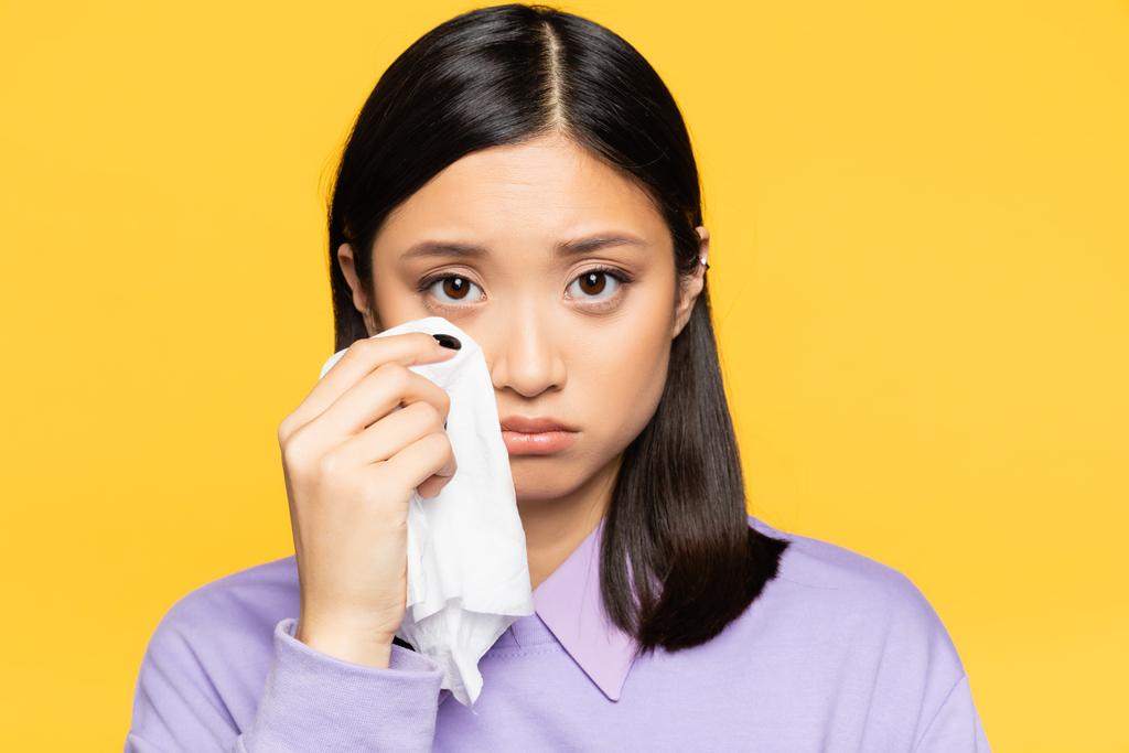 traurige asiatische Frau hält Serviette, während sie weint, isoliert auf gelb  - Foto, Bild