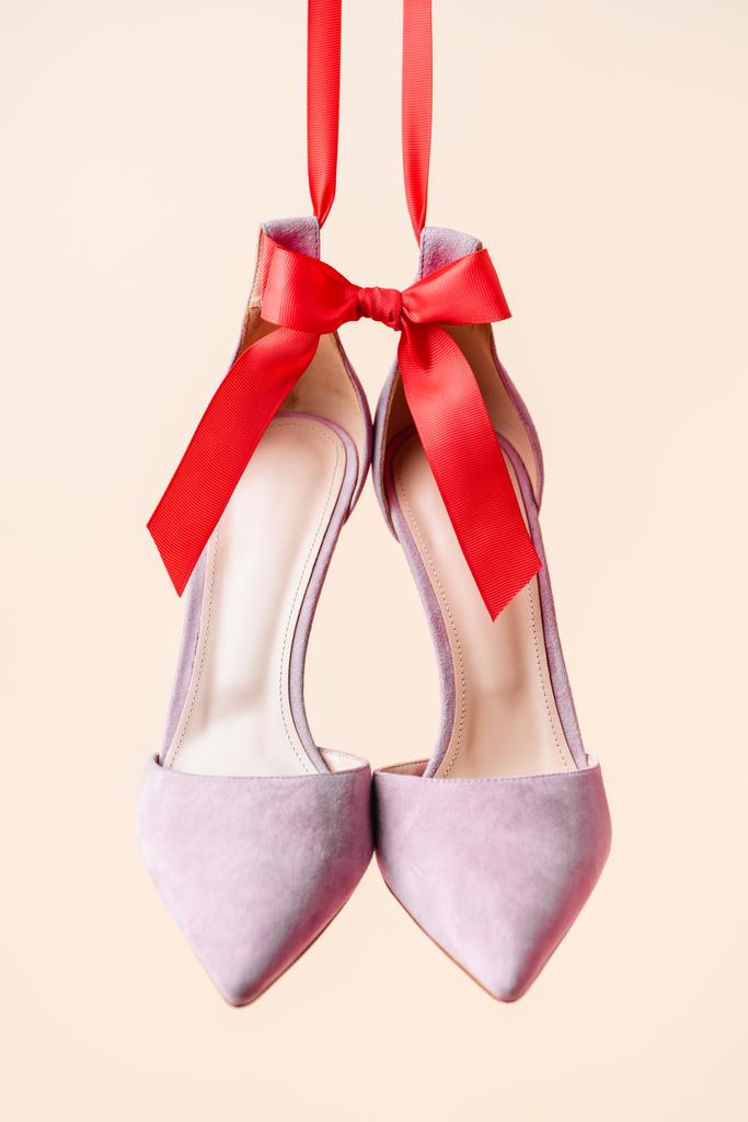lila suede hakken schoenen met rode strik geïsoleerd op beige - Foto, afbeelding
