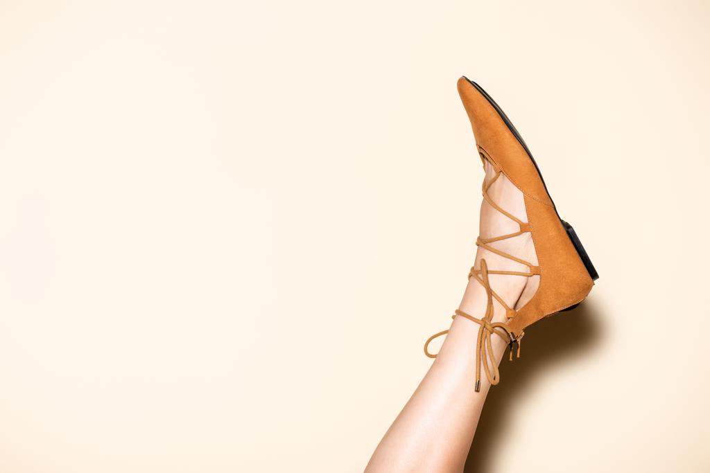 обрізаний вид жіночої ноги в коричневому замшевому пласкому взутті на бежевому фоні
 - Фото, зображення