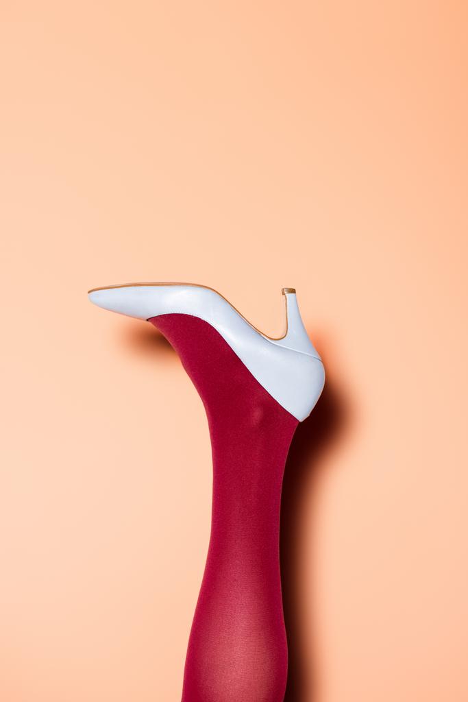 cropped view of female leg in red tights and blue shoes on peach background - Photo, Image