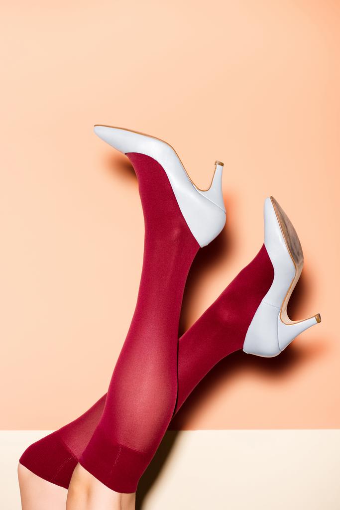 ořezaný pohled na ženské nohy v červených ponožkách a modré obuvi na broskvovém pozadí - Fotografie, Obrázek