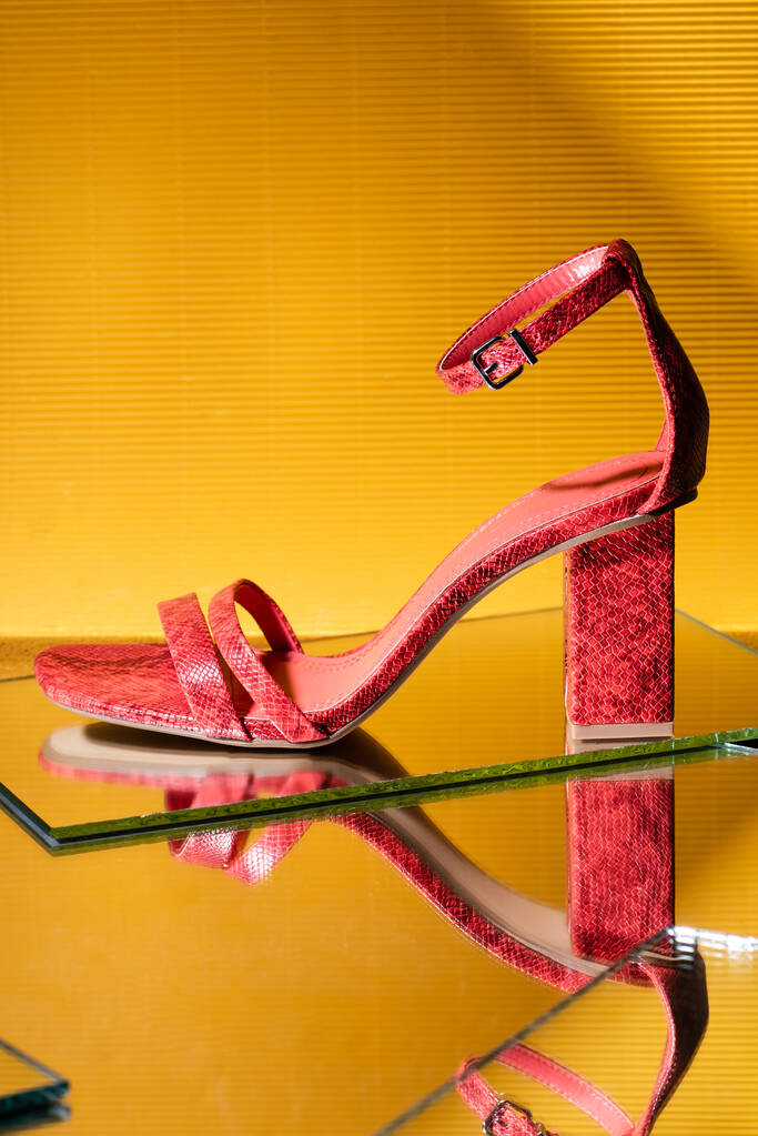 elegant pink snakeskin heeled sandals on mirror surface on yellow background - Photo, Image