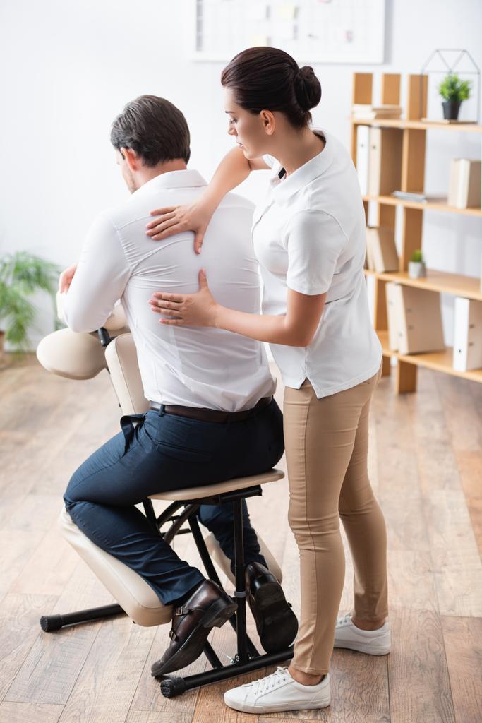 Masseuse faire assis massage sur le dos de l'homme d'affaires au bureau sur fond flou - Photo, image