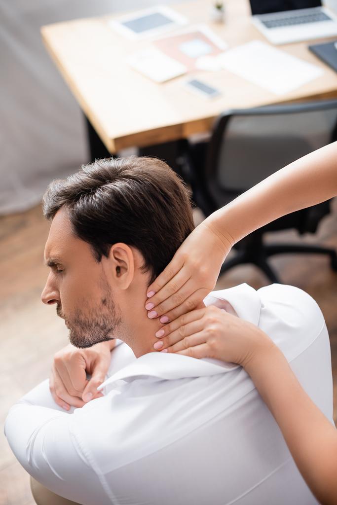 Visão aérea da massagista massageando o pescoço doloroso do empresário no escritório no fundo borrado - Foto, Imagem