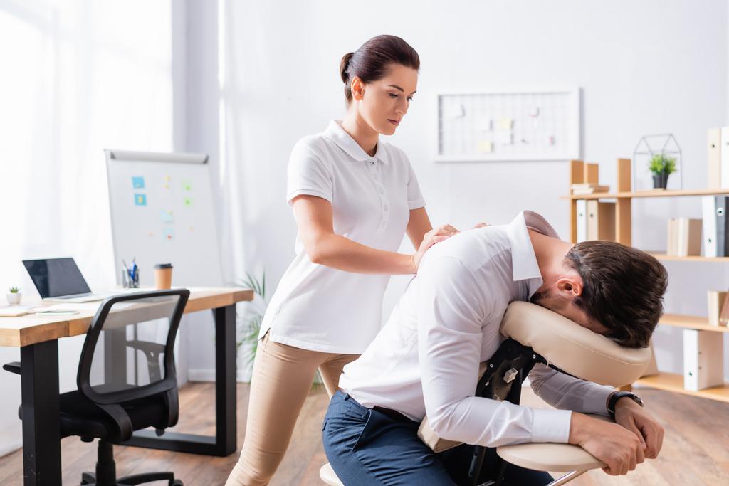 Masseuse doing seated massage of businessman back in office - Photo, Image