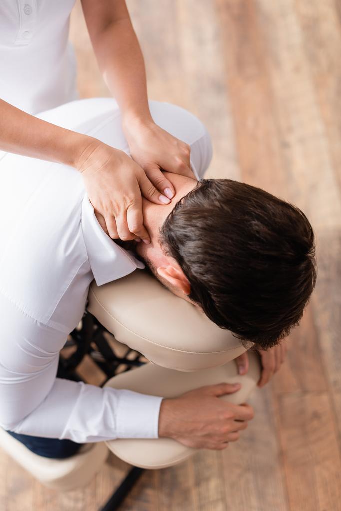 Vista aérea de masajista haciendo masaje sentado del cuello del cliente - Foto, Imagen
