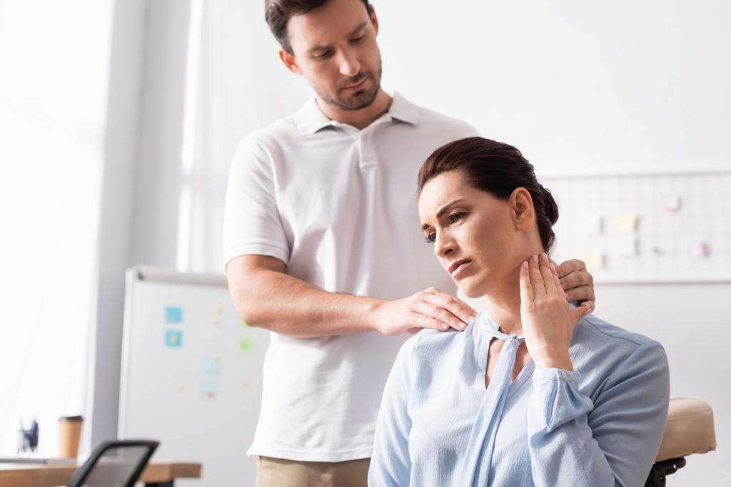 Massothérapeute massant le cou douloureux de la femme d'affaires avec bureau flou sur fond - Photo, image