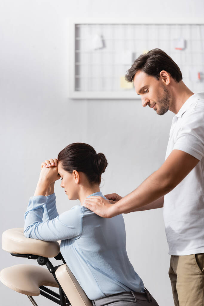Smiling masseur doing seated massage of businesswoman shoulders in office on blurred background - Photo, Image