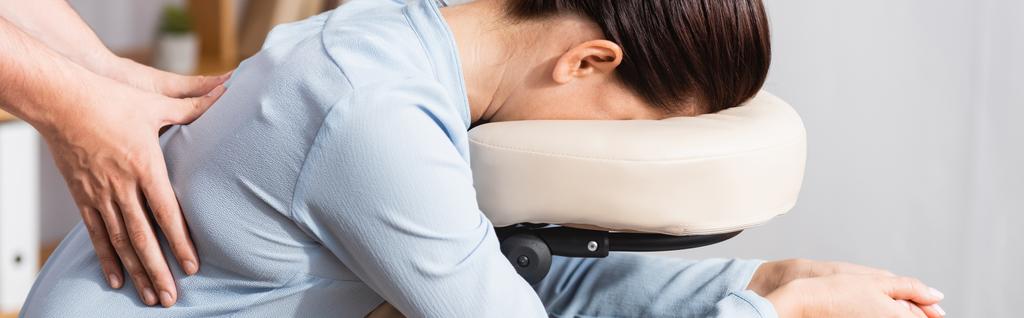 Вид сбоку массажера, делающего сидячий массаж спины для брюнетки женщины на размытом фоне, баннер - Фото, изображение