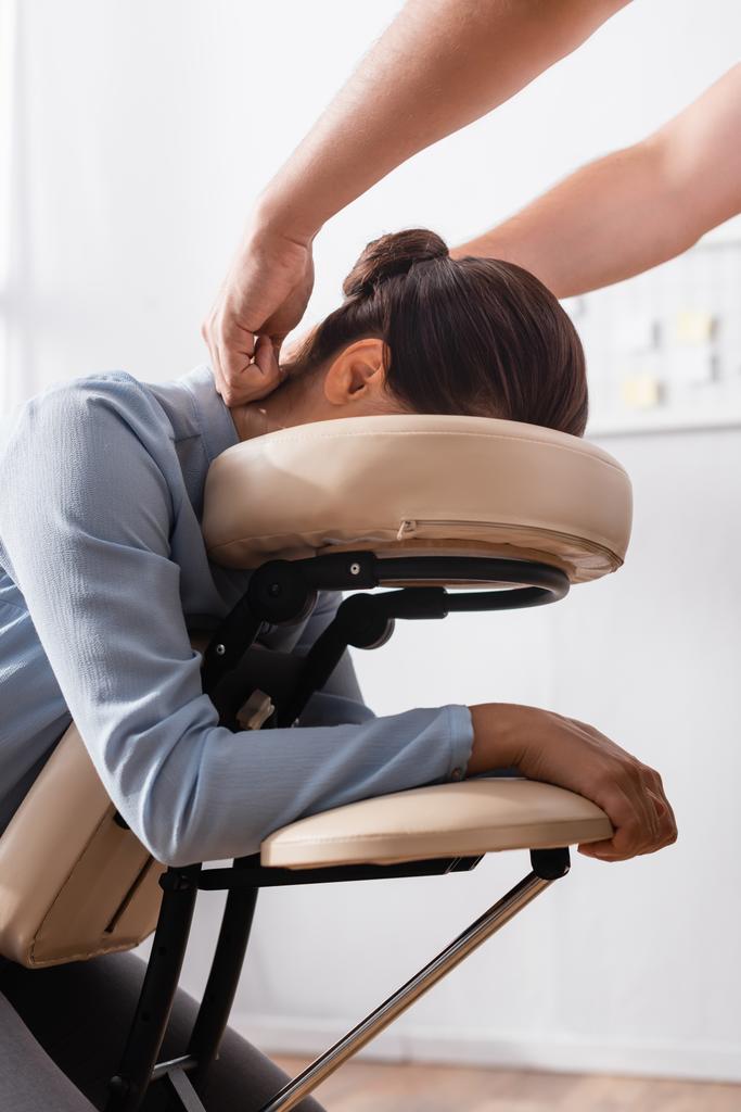 Массажист делает сидячий массаж шеи для брюнетки бизнесвумен на размытом фоне - Фото, изображение