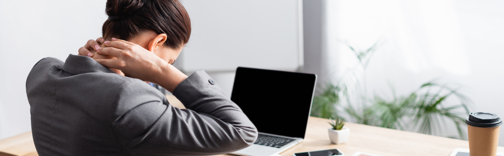 Back view of female office worker with hurting neck sitting at desk with laptop on blurred background, banner - Photo, Image