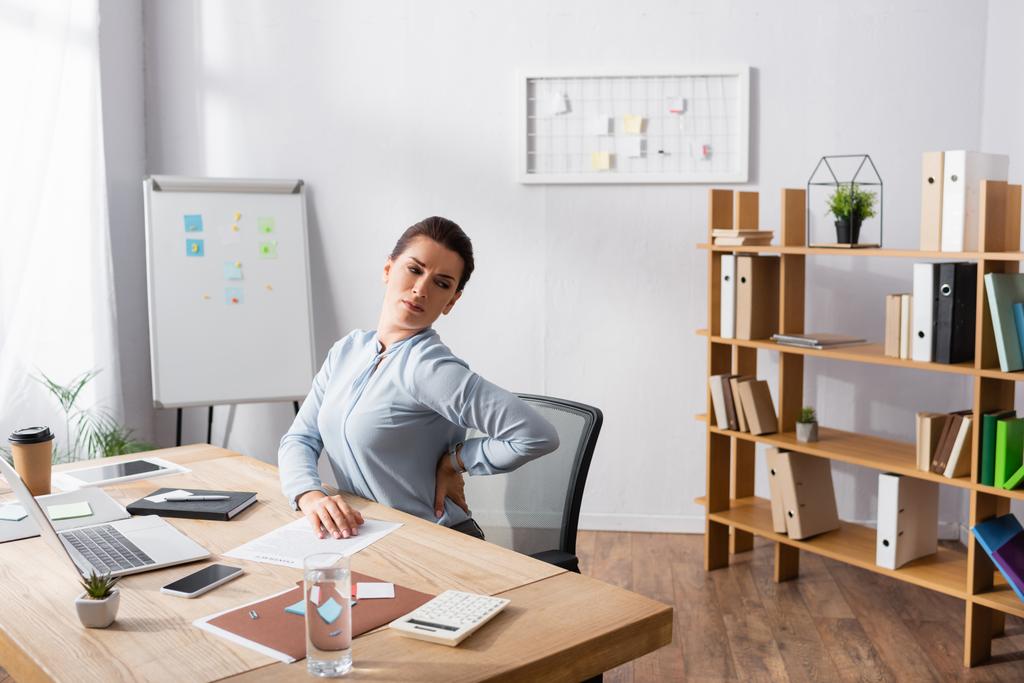 Mulher com dor nas costas sentado com a mão no quadril no local de trabalho no escritório - Foto, Imagem