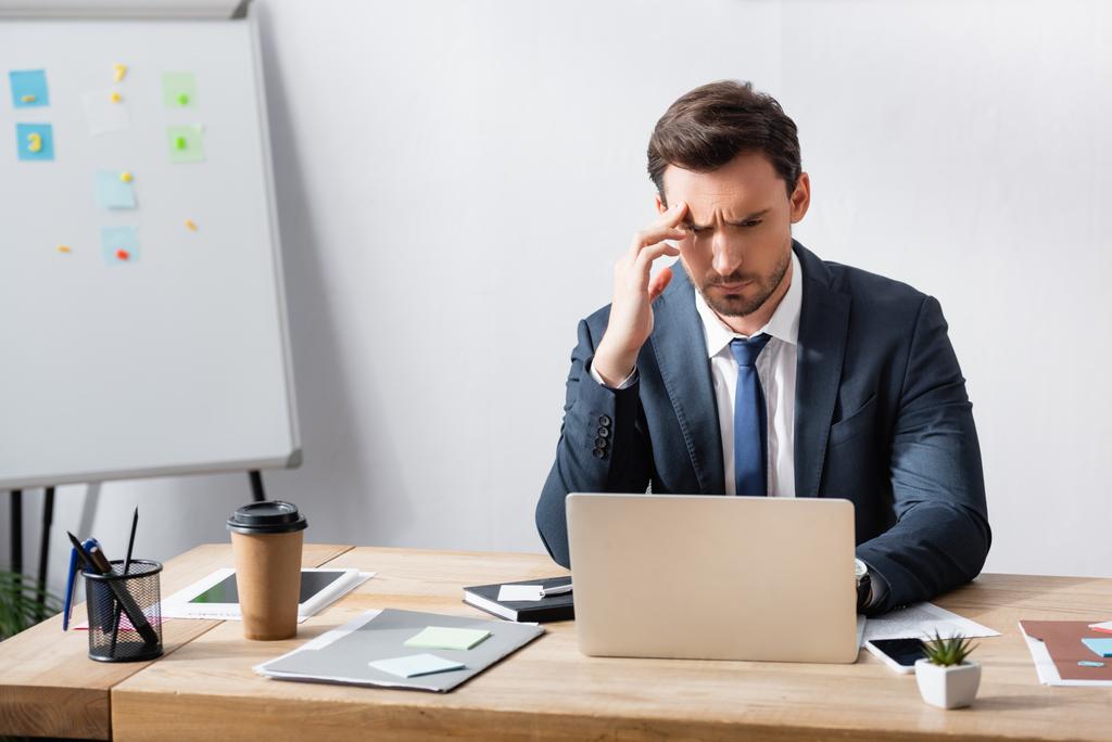Liikemies migreeni katselee kannettavaa tietokonetta istuessaan työpaikalla lähellä flipchart - Valokuva, kuva