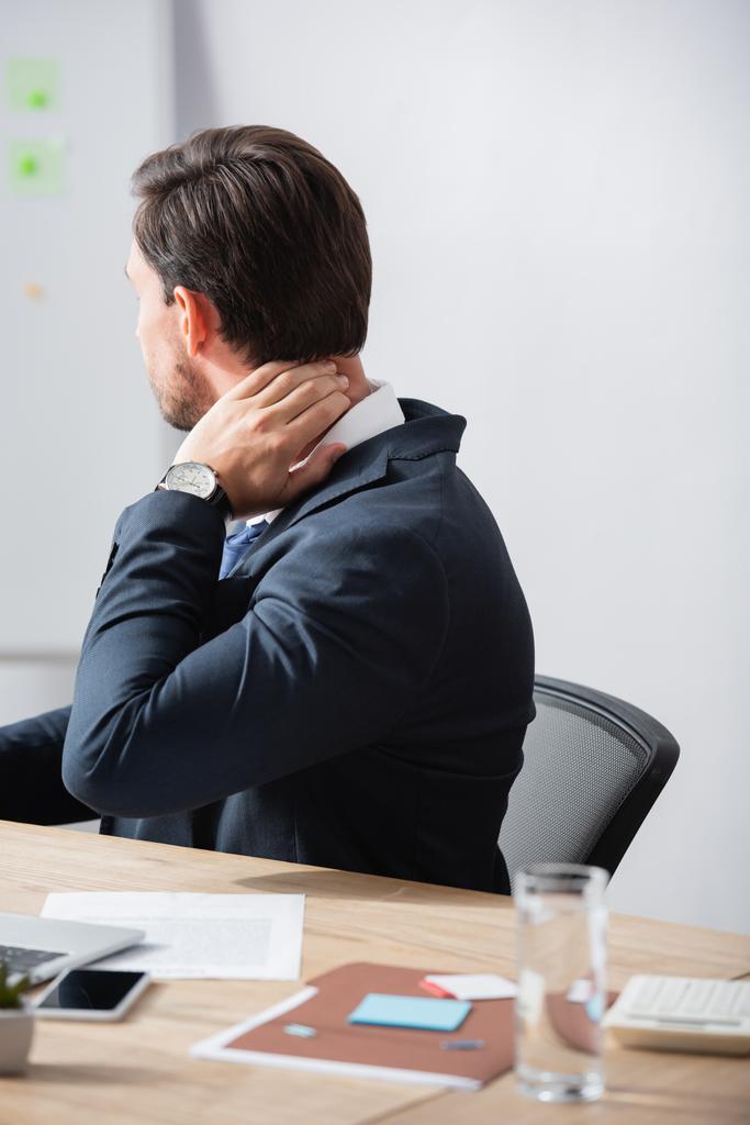 Trabajador de oficina con el cuello doloroso sentado en el lugar de trabajo sobre fondo borroso - Foto, Imagen