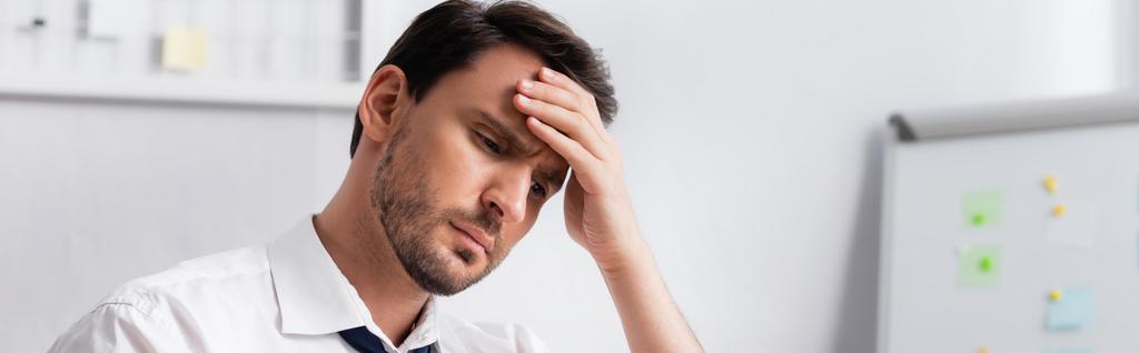 Exhausted businessman with migraine holding hand on forehead, while looking away on blurred background, banner - Photo, Image
