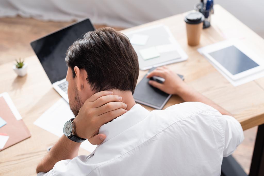 Visão traseira do trabalhador de escritório com dor no pescoço sentado no local de trabalho no fundo embaçado - Foto, Imagem