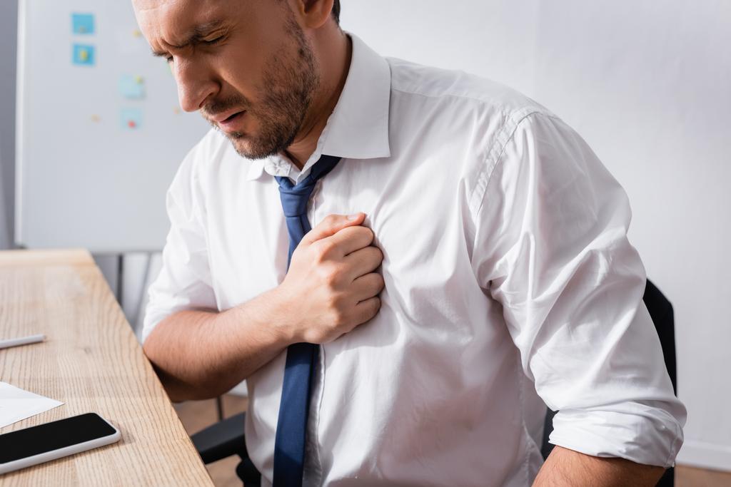 Podnikatel má infarkt, zatímco sedí na pracovišti na rozmazaném pozadí - Fotografie, Obrázek