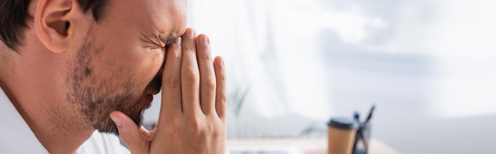 Вид збоку виснаженого офісного працівника з молитовними руками, який страждає від мігрені на розмитому тлі, банер
 - Фото, зображення