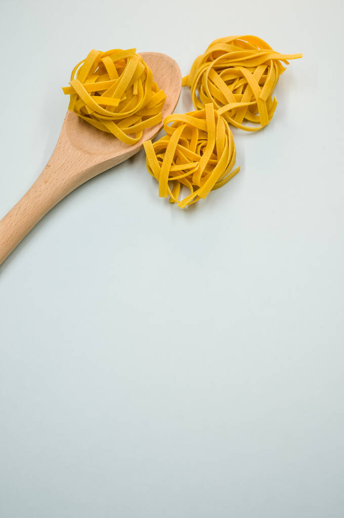 A vertical shot of tagliatelle pasta and a wooden kitchen tool - Photo, Image