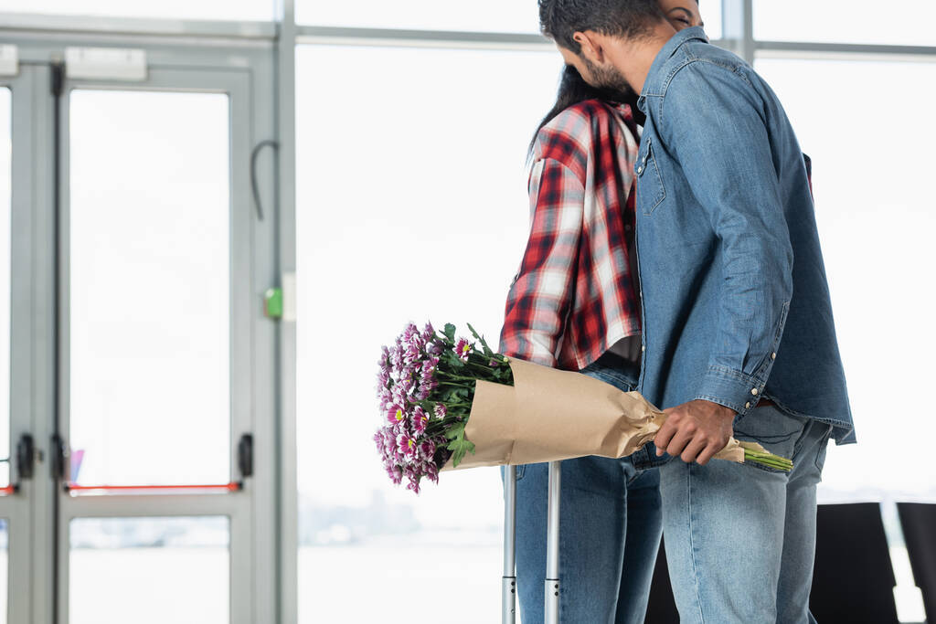 man holding verpakt bloemen terwijl vergadering Afrikaans amerikaans vriendin in luchthaven - Foto, afbeelding