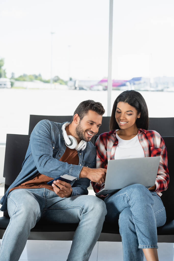весела міжрасова пара дивиться на ноутбук в аеропорту
  - Фото, зображення