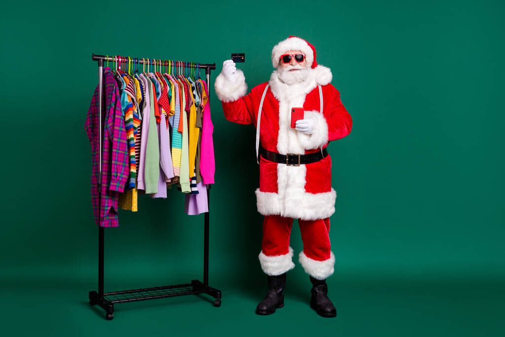 Täysikokoinen kuva valkoiset hiukset joulupukki käyttää matkapuhelin ostaja shopper x-mas aattona kausi alennus maksaa luottokortti vaatekaappi vaatteet kulumista punainen puku saappaat vyö korkki eristetty vihreä väri tausta - Valokuva, kuva