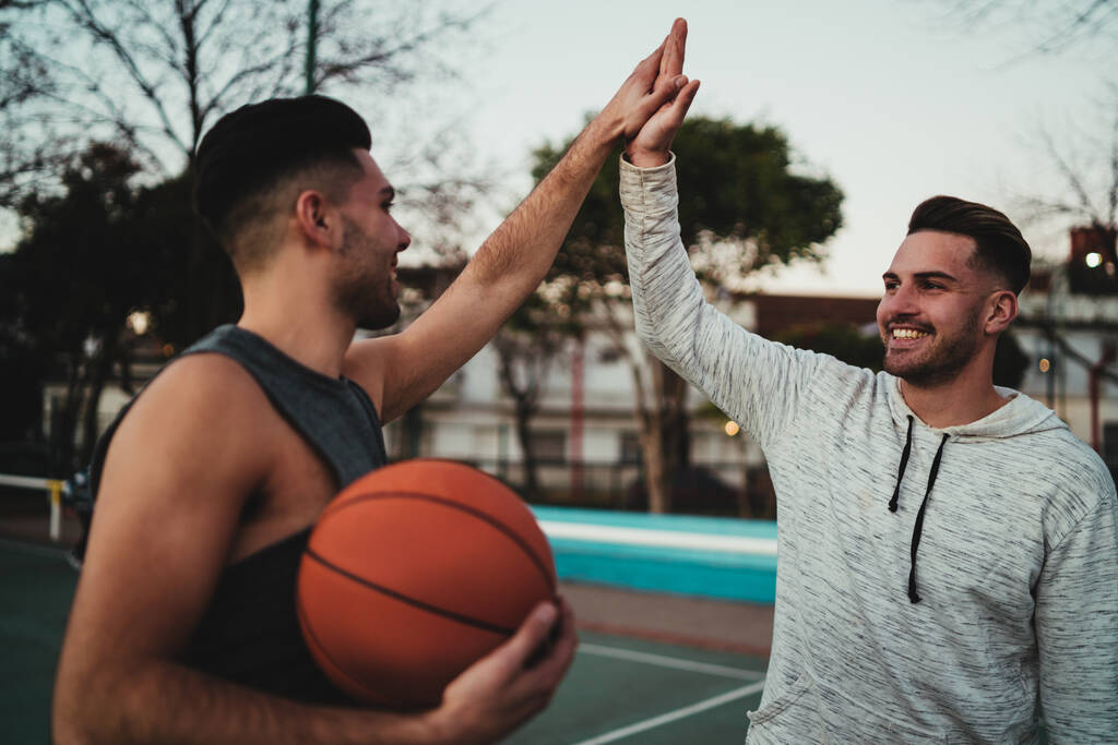 Muotokuva kahdesta nuoresta kaverista pelaamassa koripalloa ja pitämässä hauskaa kentällä ulkona. Urheilukäsite. - Valokuva, kuva