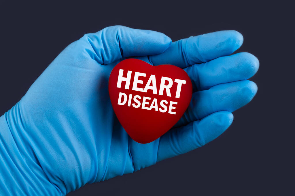 Arzt in blauen Handschuhen hält ein Herz mit Text Herzkrankheit, Konzept. - Foto, Bild