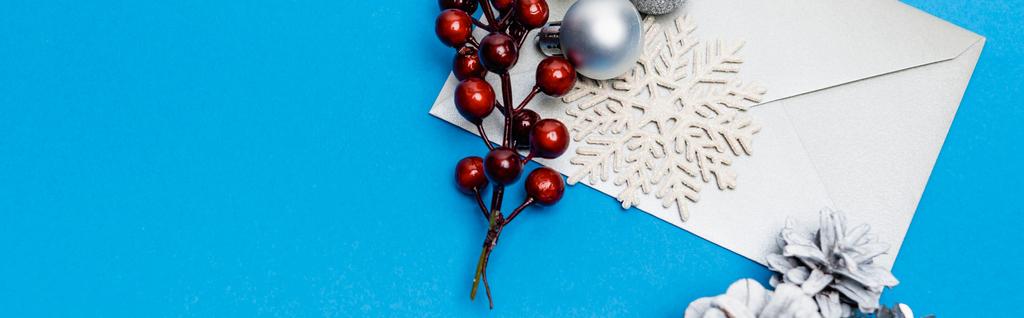top view of snowflake, silver baubles, berries and envelope on blue background, banner - Photo, Image