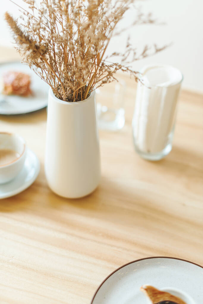 Λευκά πιάτα σε στυλ μιλιταρισμού στο τραπέζι με αποξηραμένα λουλούδια στο βάζο στο καφέ - Φωτογραφία, εικόνα