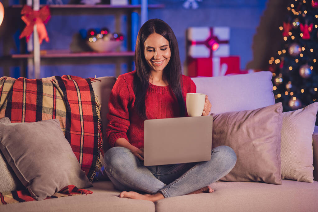 Photo portrait of woman sitting on sofa in lotus pose with laptop mug with christmas decorations indoors - Photo, Image