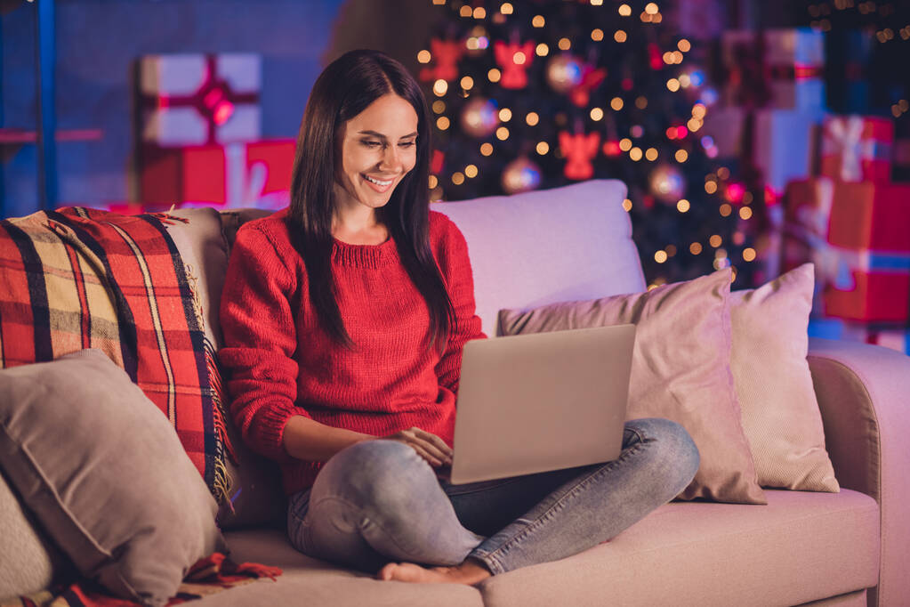 Fotoporträt einer Frau auf Sofa in Lotus-Pose mit Laptop mit Weihnachtsdekoration im Inneren - Foto, Bild