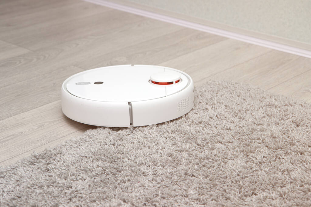 aspiradora Robot blanco conduce en la alfombra. Superar los obstáculos con la aspiradora robot. limpieza ideal de la casa con modernos electrodomésticos inalámbricos. concepto de hogar inteligente. - Foto, Imagen
