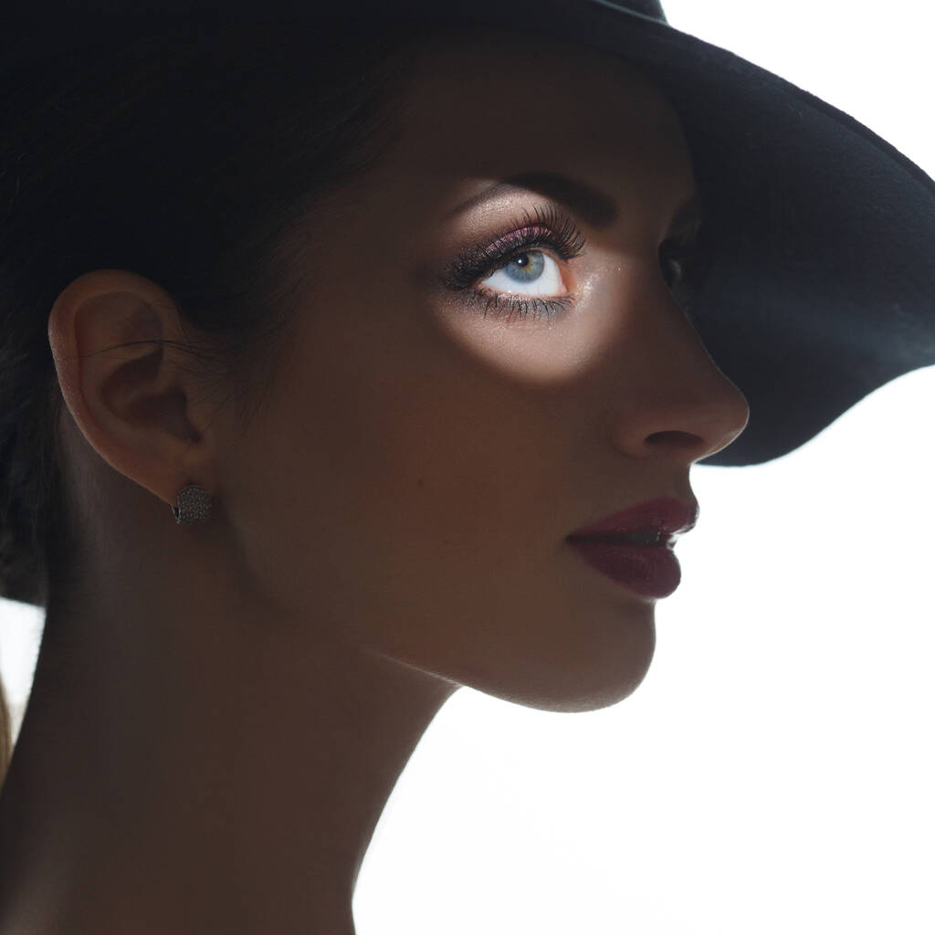 Mysterious silhouette portrait of a beautiful girl in an elegant hat with a light focus on the eye, isolated on a white background. - Photo, Image