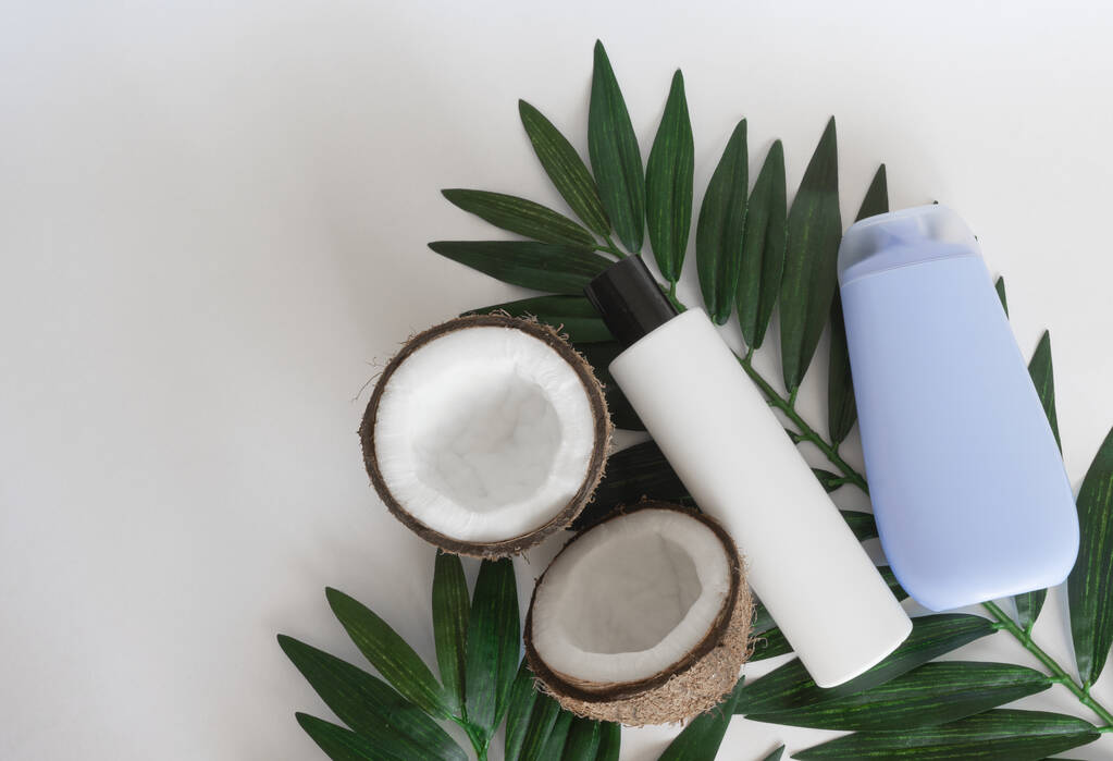 ココナッツの半分と熱帯の葉と白い背景に有機製品から健康な髪のためのシャンプーの2種類。生態製品の概念。上からの眺め。スペースのコピー - 写真・画像