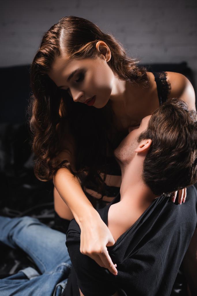 Sensual woman taking off t-shirt from boyfriend on bed  - Photo, Image