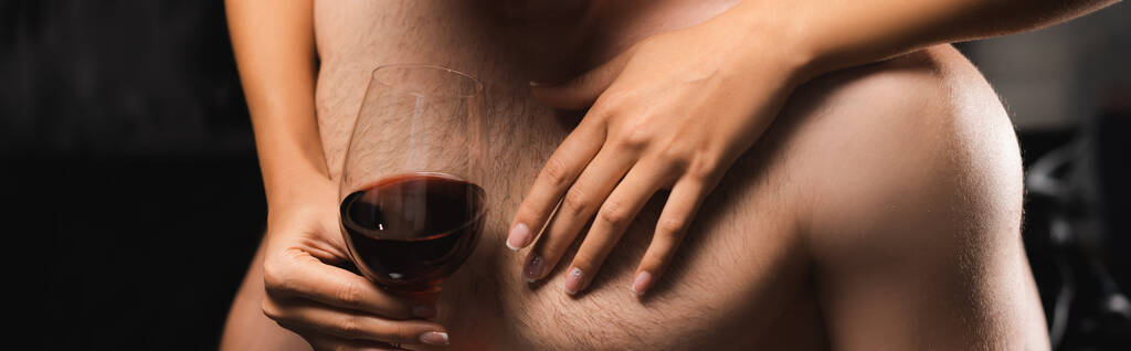 Ausgeschnittene Ansicht einer Frau mit einem Glas Wein, das die Brust ihres hemdslosen Freundes berührt, Banner  - Foto, Bild