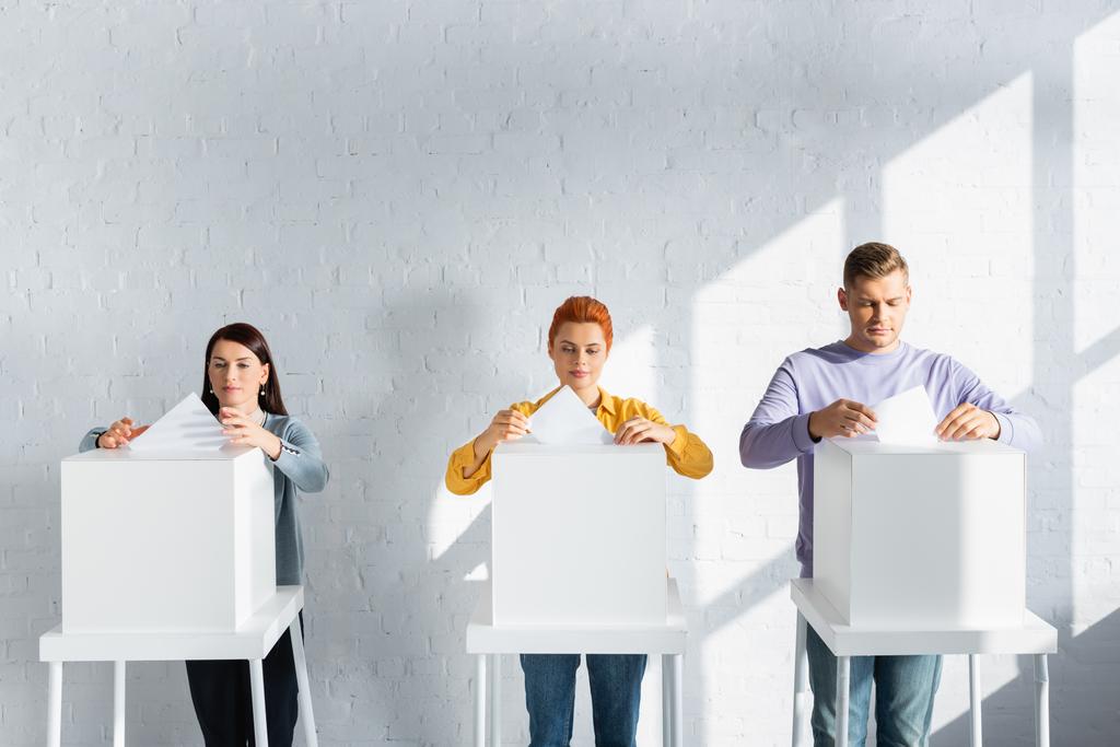 äänestäjät, jotka asettavat äänestysliput äänestyslaatikoihin valkoista tiiliseinää vasten - Valokuva, kuva