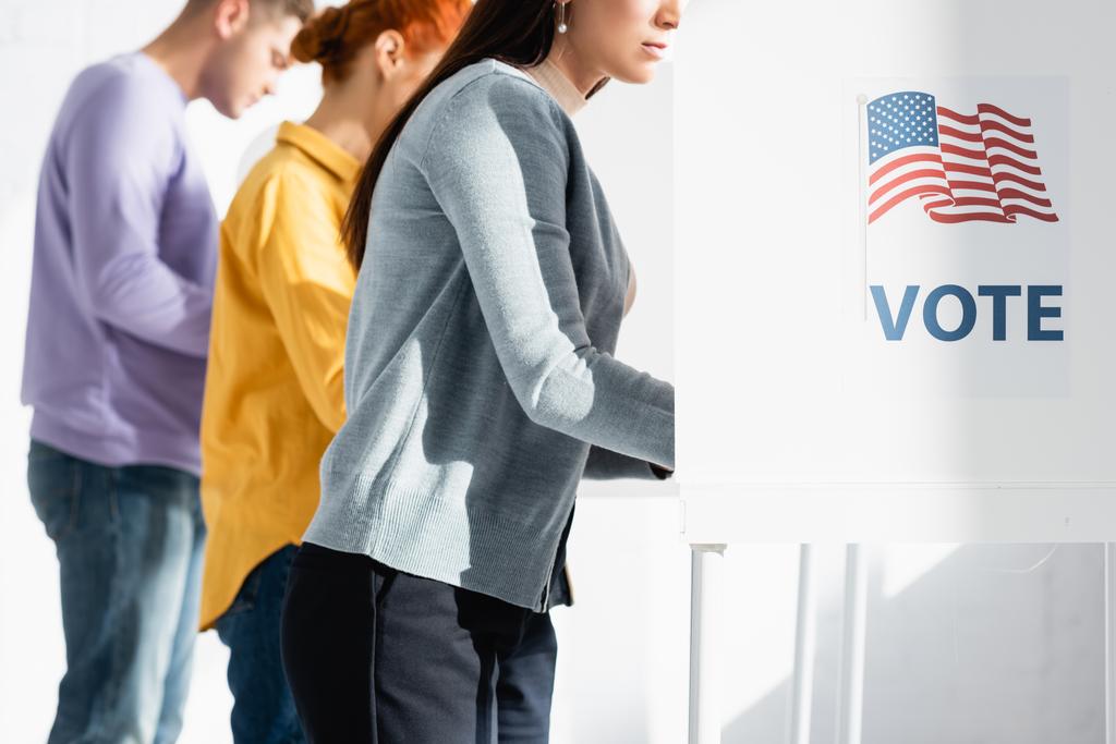 voters in polling booths with american flag and vote inscription on blurred background - Photo, Image